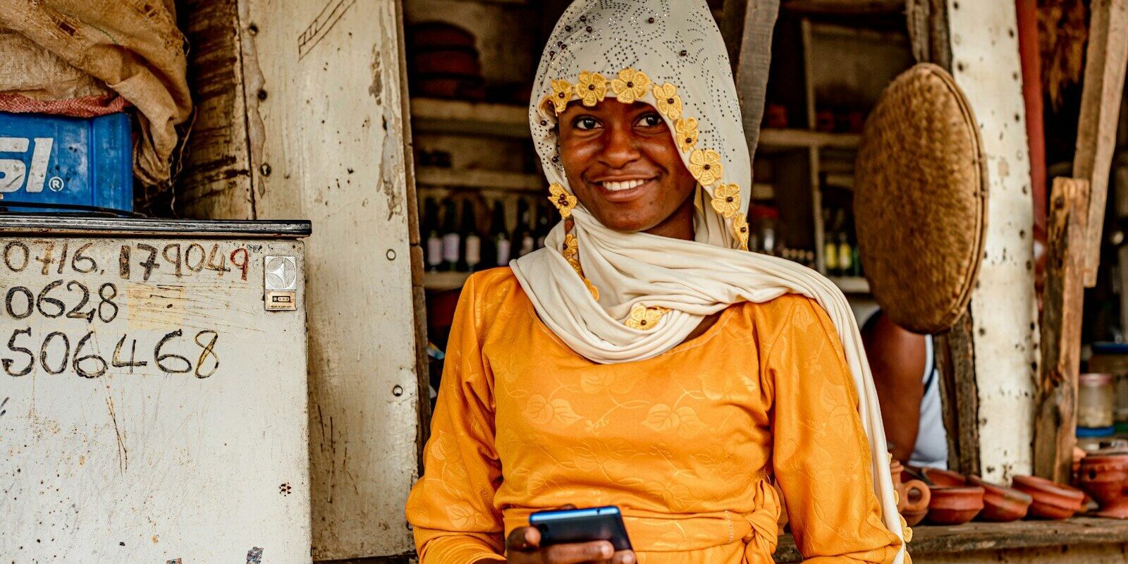 Kenyan shopkeeper using her phone at her shop counter, representing small business compliance with eTIMS electronic tax invoicing