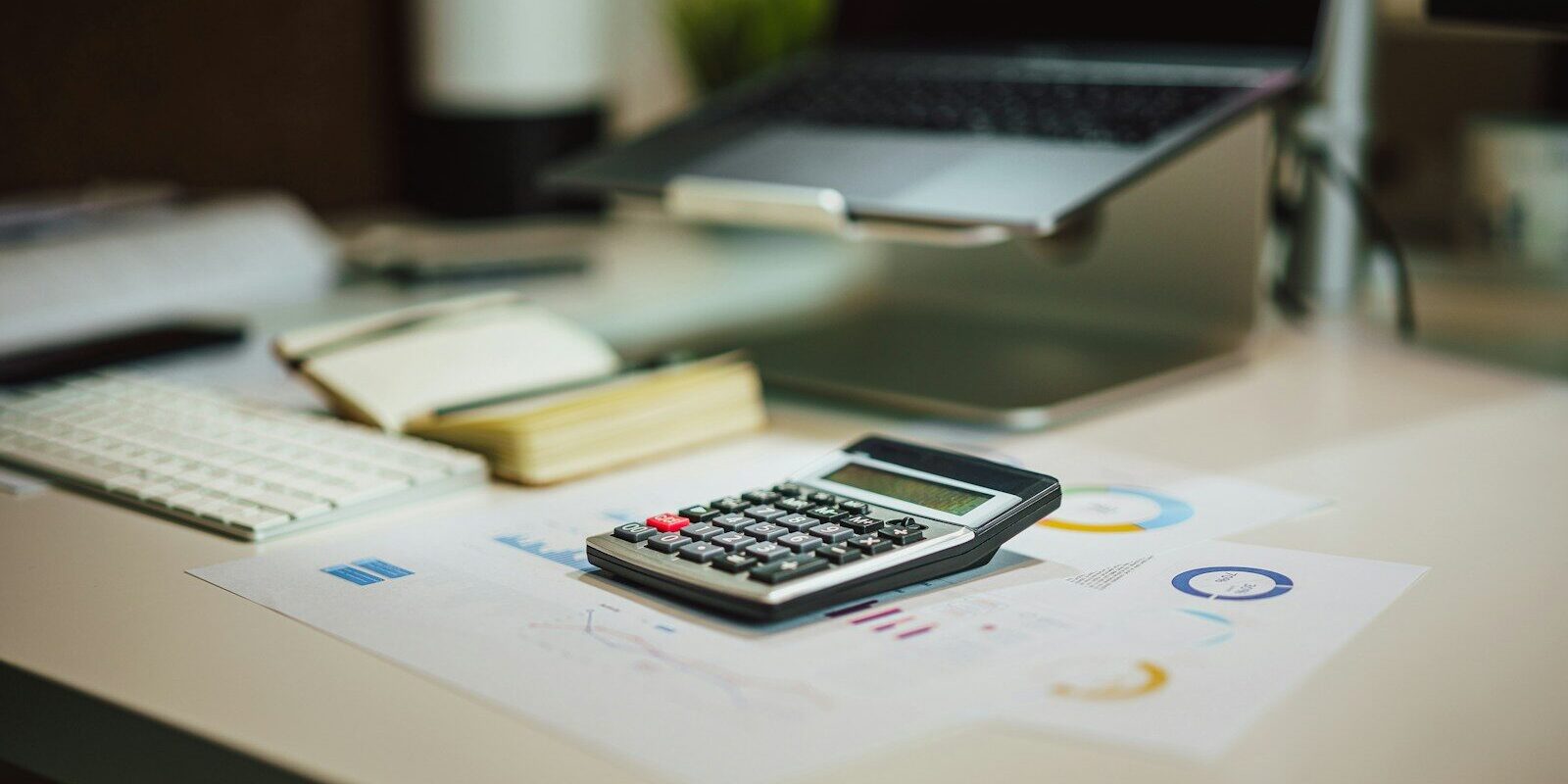 A calculator and financial charts on an office desk, representing the transaction monitoring work behind an anti-money laundering compliance programme.