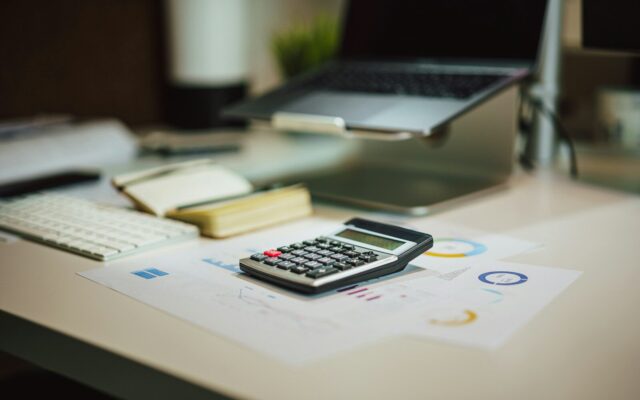 A calculator and financial charts on an office desk, representing the transaction monitoring work behind an anti-money laundering compliance programme.