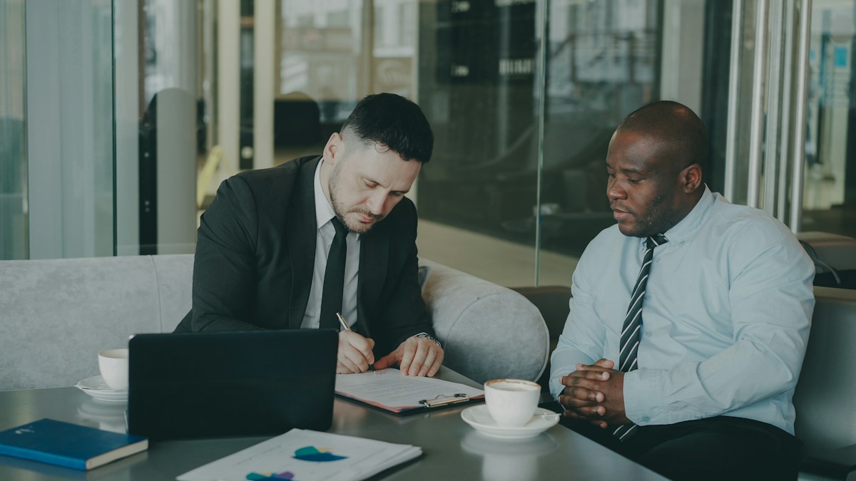 Two businessmen reviewing and signing an acquisition document, representing change of control approvals for acquiring a licensed financial services business in Kenya