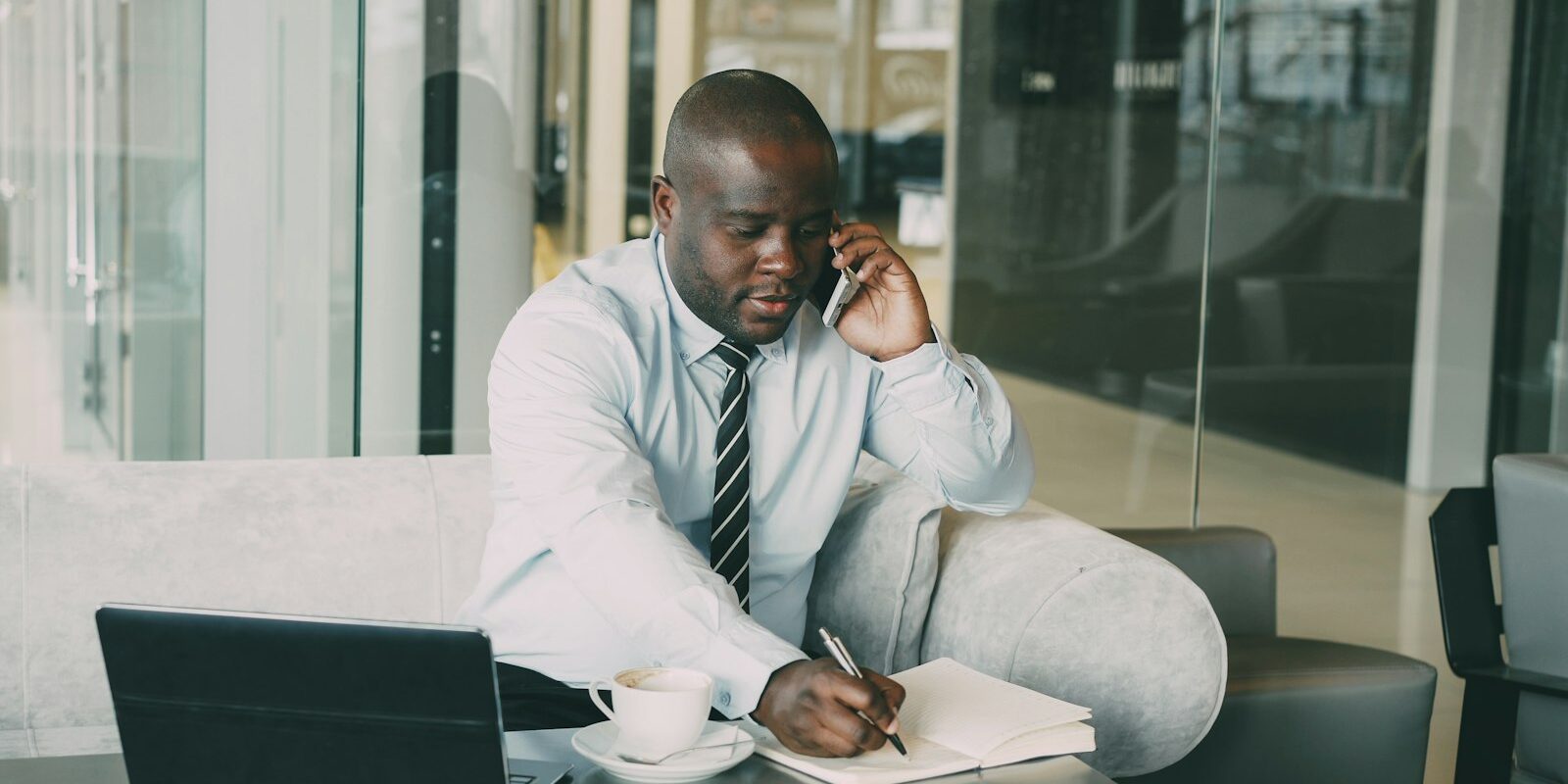 African manager on the phone taking notes at a desk while reviewing a staff code of conduct