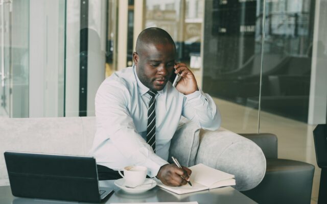 African manager on the phone taking notes at a desk while reviewing a staff code of conduct