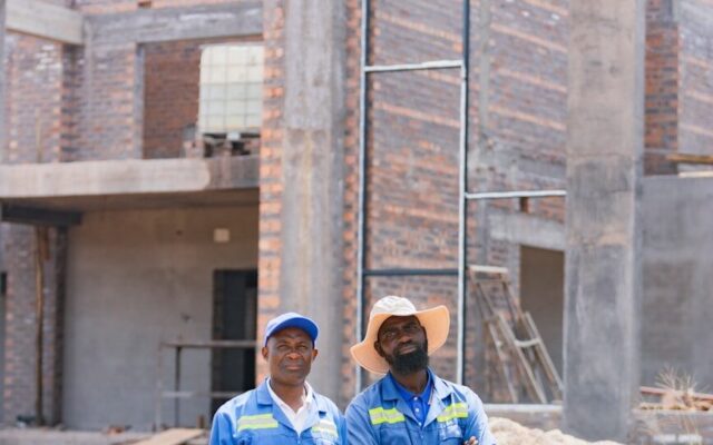 Two African construction workers in blue coveralls standing at a special economic zone development site in Kenya