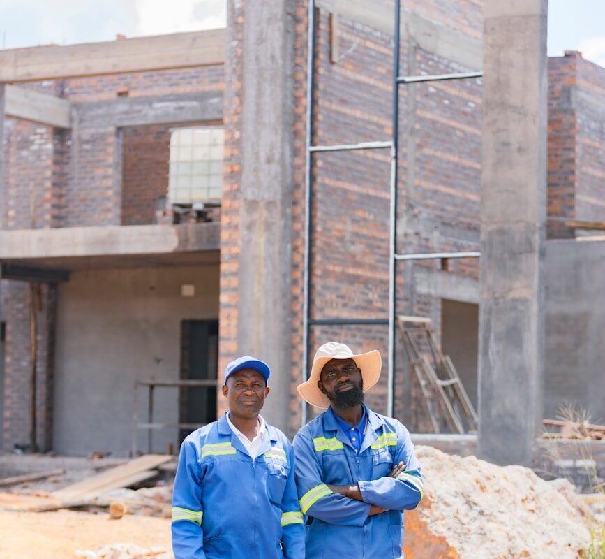 Two African construction workers in blue coveralls standing at a special economic zone development site in Kenya