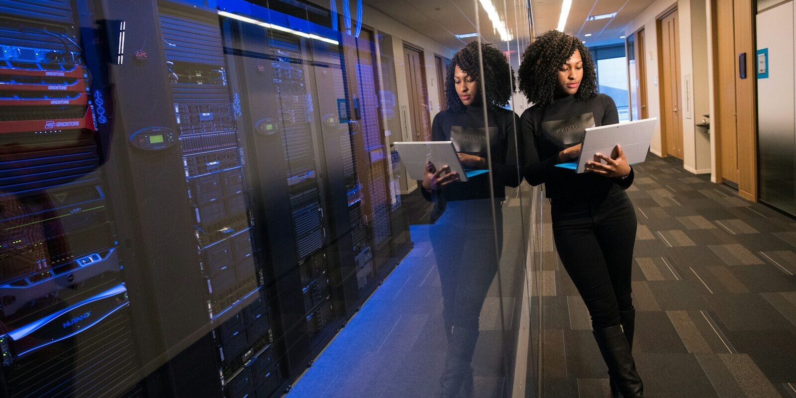 A cybersecurity professional reviewing data on a tablet beside a server rack, representing the technical infrastructure regulated under Kenya’s new National Cybersecurity Agency Order.