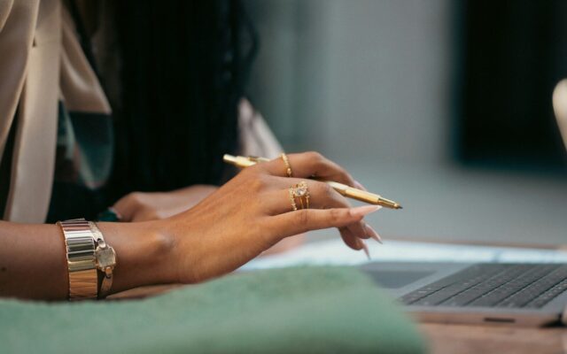 Company name reservation versus trademark protection: African businesswoman with gold pen and laptop reviewing brand name records