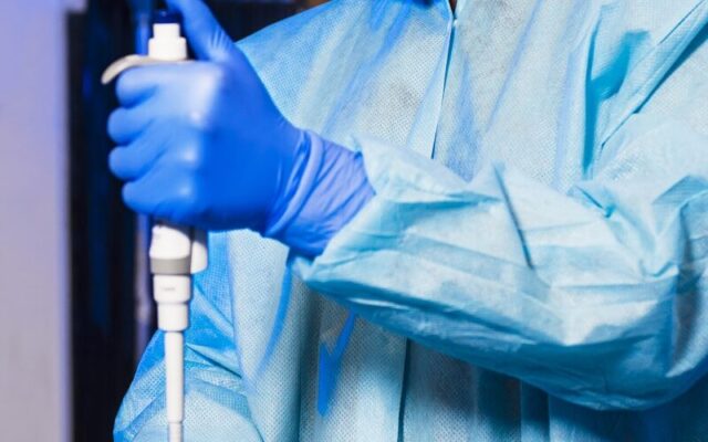Generic Drug Manufacturer Registration Kenya — Scientist in a gown and gloves using a pipette among vials in a pharmaceutical laboratory