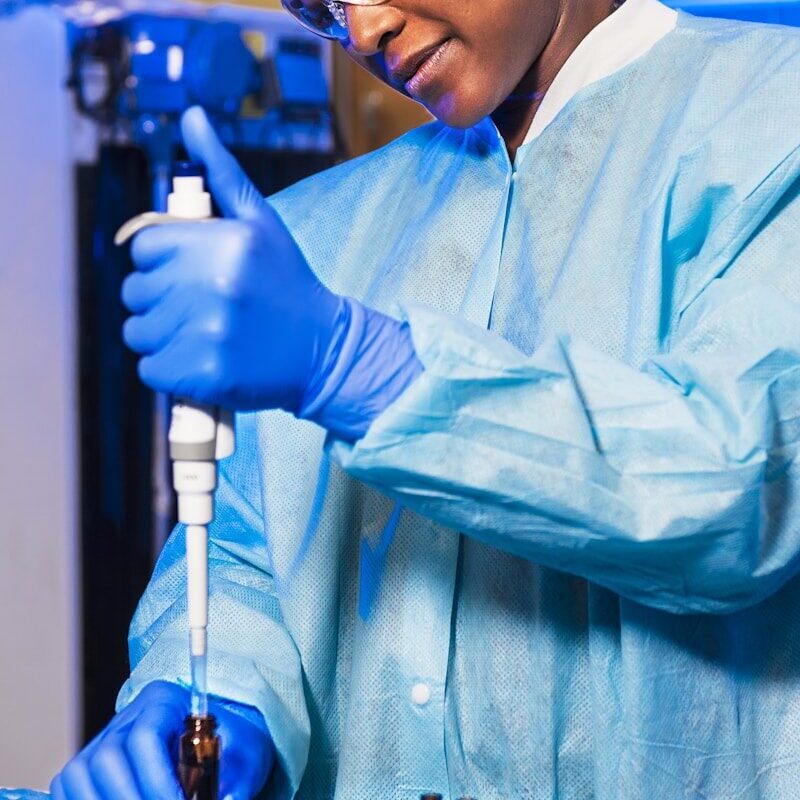 Generic Drug Manufacturer Registration Kenya — Scientist in a gown and gloves using a pipette among vials in a pharmaceutical laboratory