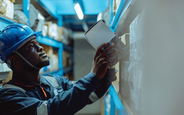 Medical Device Distribution Business Kenya — African warehouse worker in a hard hat checking inventory against a shipment