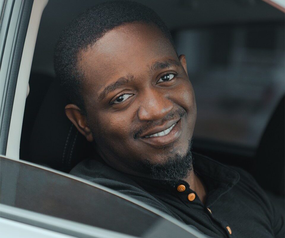 African ride-hailing driver smiling at the camera from inside his car, representing the employment classification question for Uber and Bolt drivers in Kenya