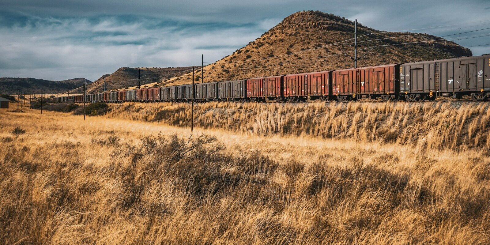 Freight train hauling cargo wagons across grassland near hills, representing goods transported under Kenya's Railway Development Levy.