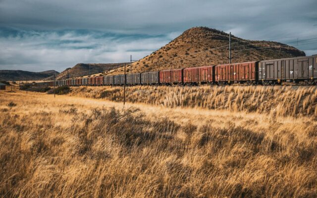 Freight train hauling cargo wagons across grassland near hills, representing goods transported under Kenya's Railway Development Levy.