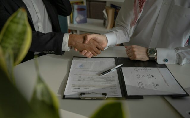 Two business people shaking hands over signed documents