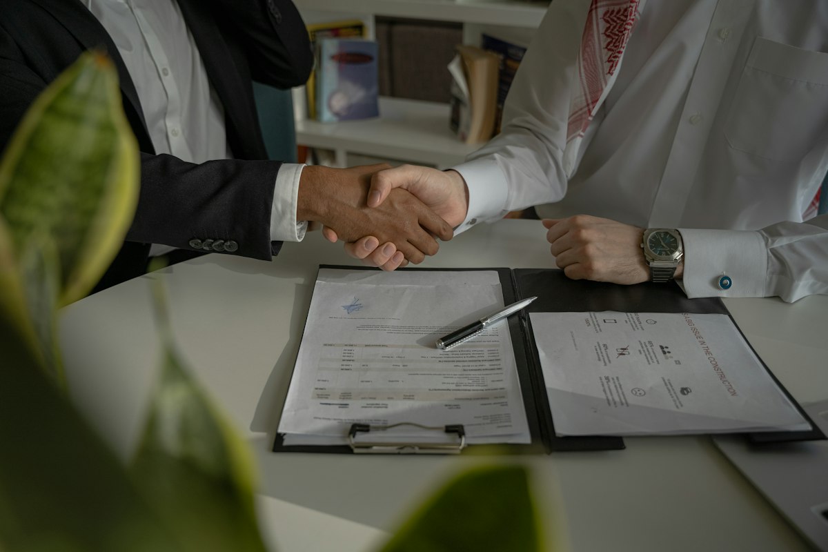 Two business people shaking hands over signed documents