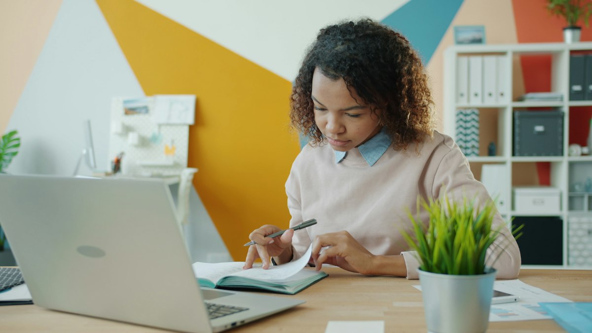 A businesswoman working at a desk with a laptop and notebook