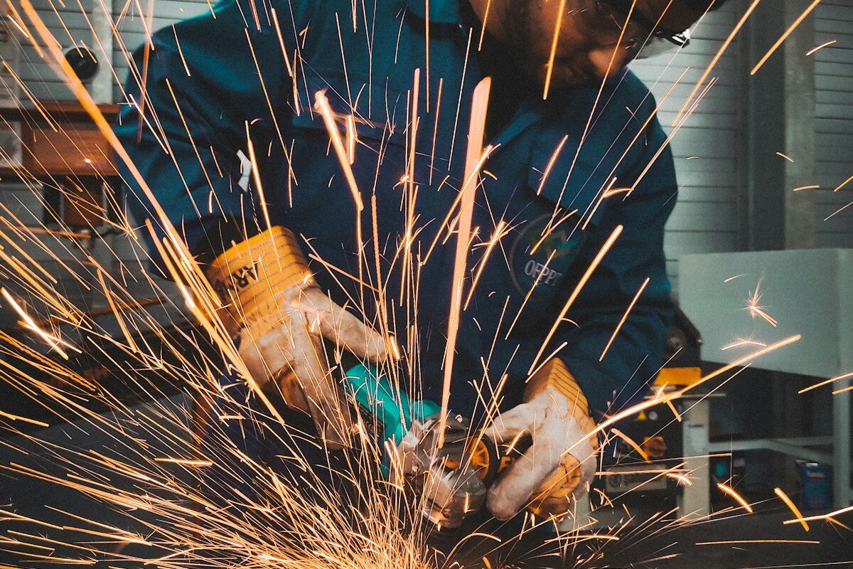 A factory worker grinding metal with sparks flying