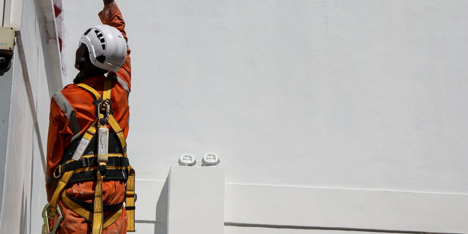 Technician in safety harness and helmet working at height on a building installation