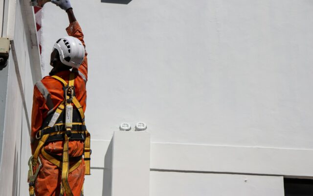 Technician in safety harness and helmet working at height on a building installation
