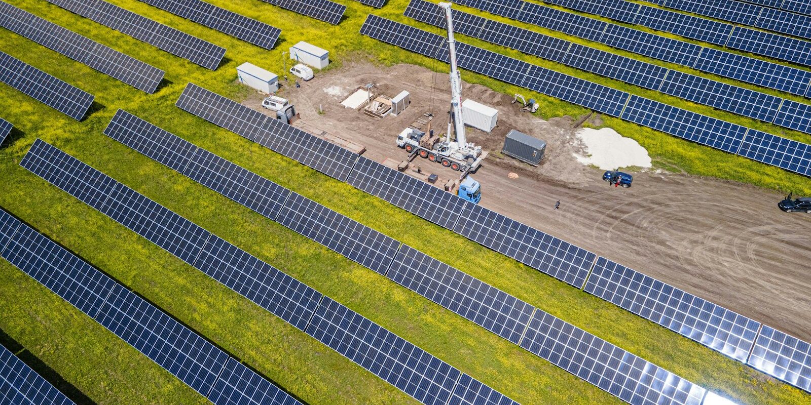Aerial view of a large solar panel field under installation with a crane