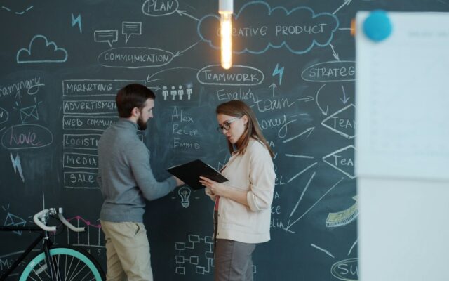 Two colleagues reviewing a business plan at a chalkboard