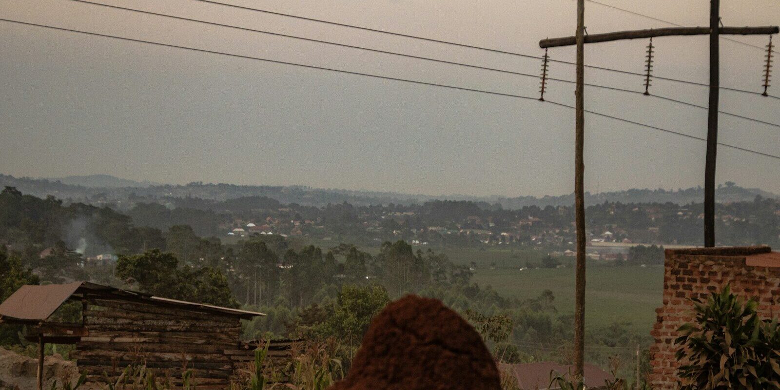 Power transmission poles and lines running across a hilly East African landscape with village rooftops, representing grid power supply for green hydrogen projects in Kenya