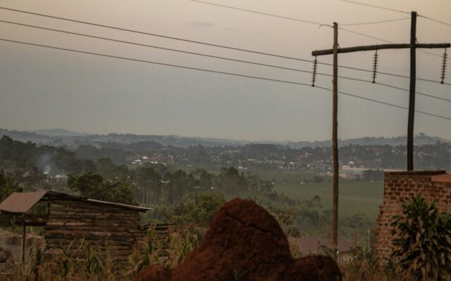 Power transmission poles and lines running across a hilly East African landscape with village rooftops, representing grid power supply for green hydrogen projects in Kenya