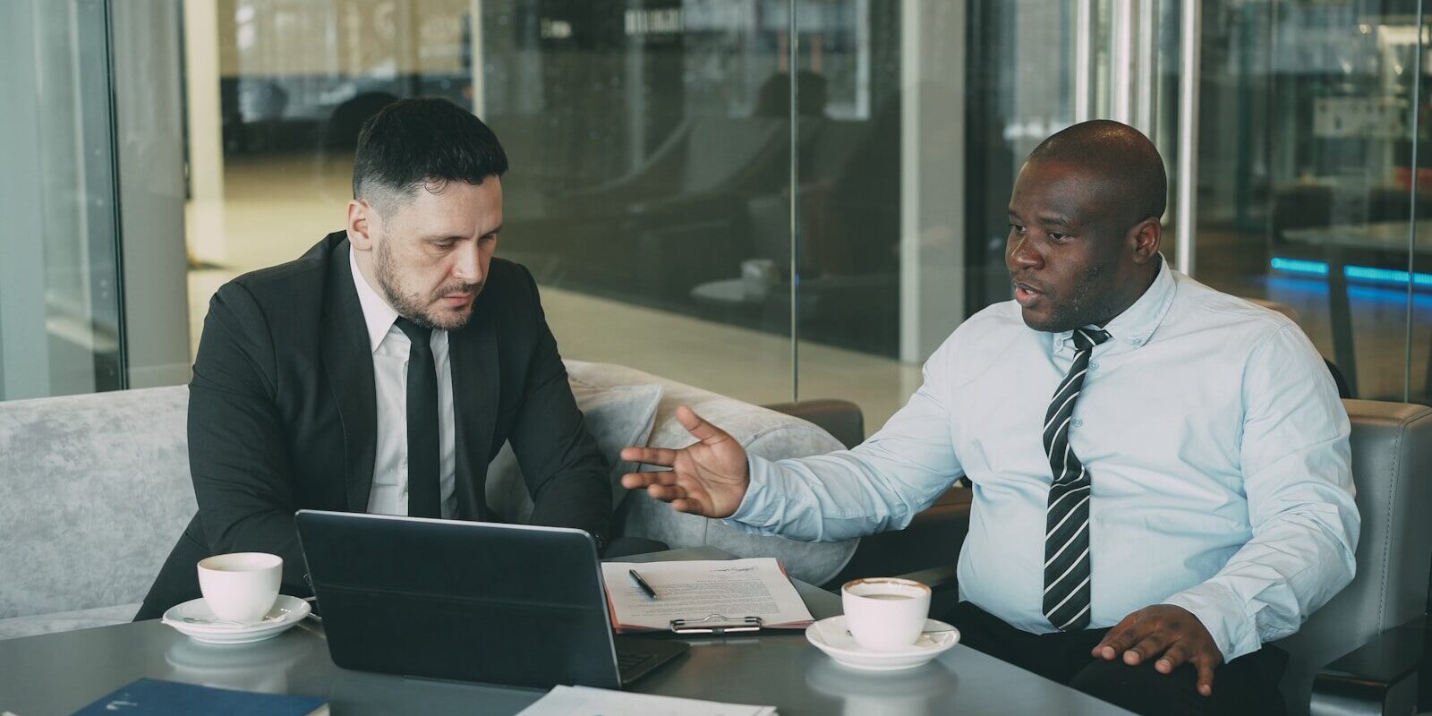 Two African business professionals shaking hands over a laptop and coffee, discussing an investment structuring agreement