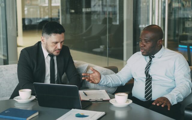 Two African business professionals shaking hands over a laptop and coffee, discussing an investment structuring agreement