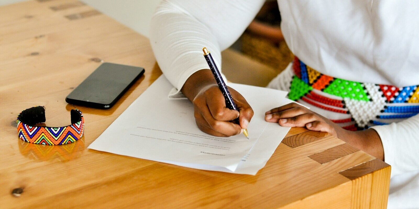 Woman signing a family trust deed at a wooden desk, wearing a Kenyan beaded bracelet
