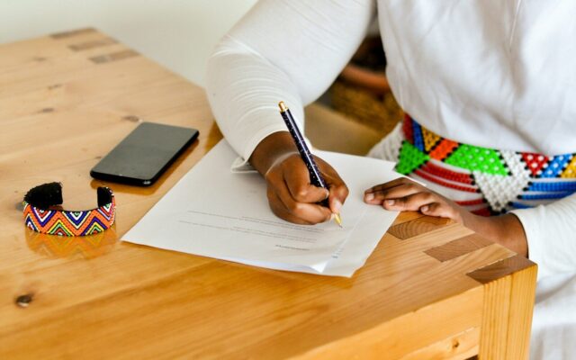 Woman signing a family trust deed at a wooden desk, wearing a Kenyan beaded bracelet