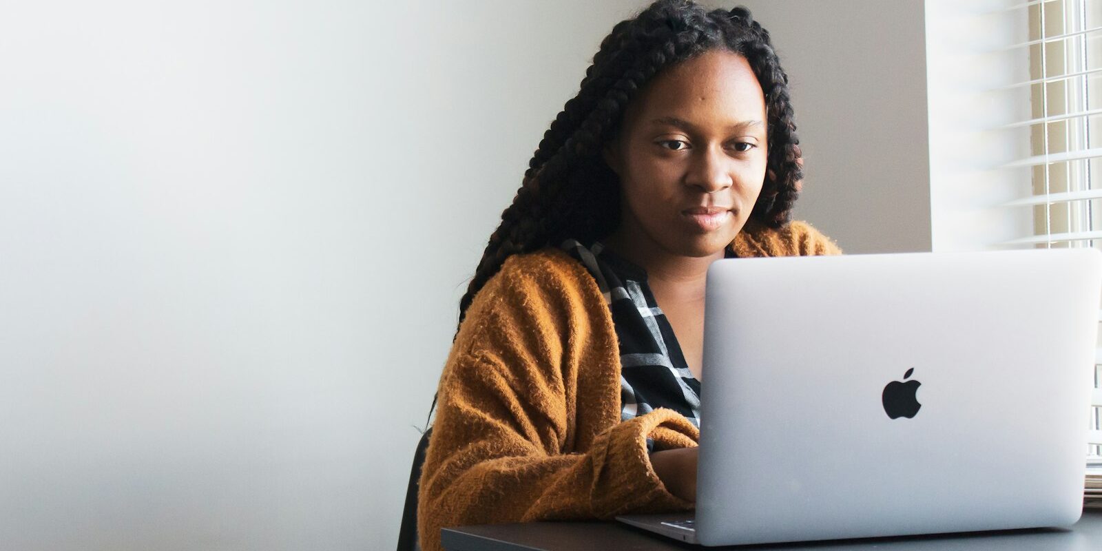 Remote worker with braided hair using a laptop at a desk by a window