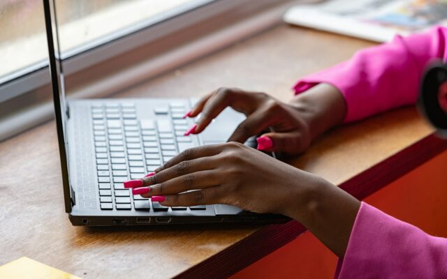 Hands typing on a laptop keyboard at a wooden desk by a window